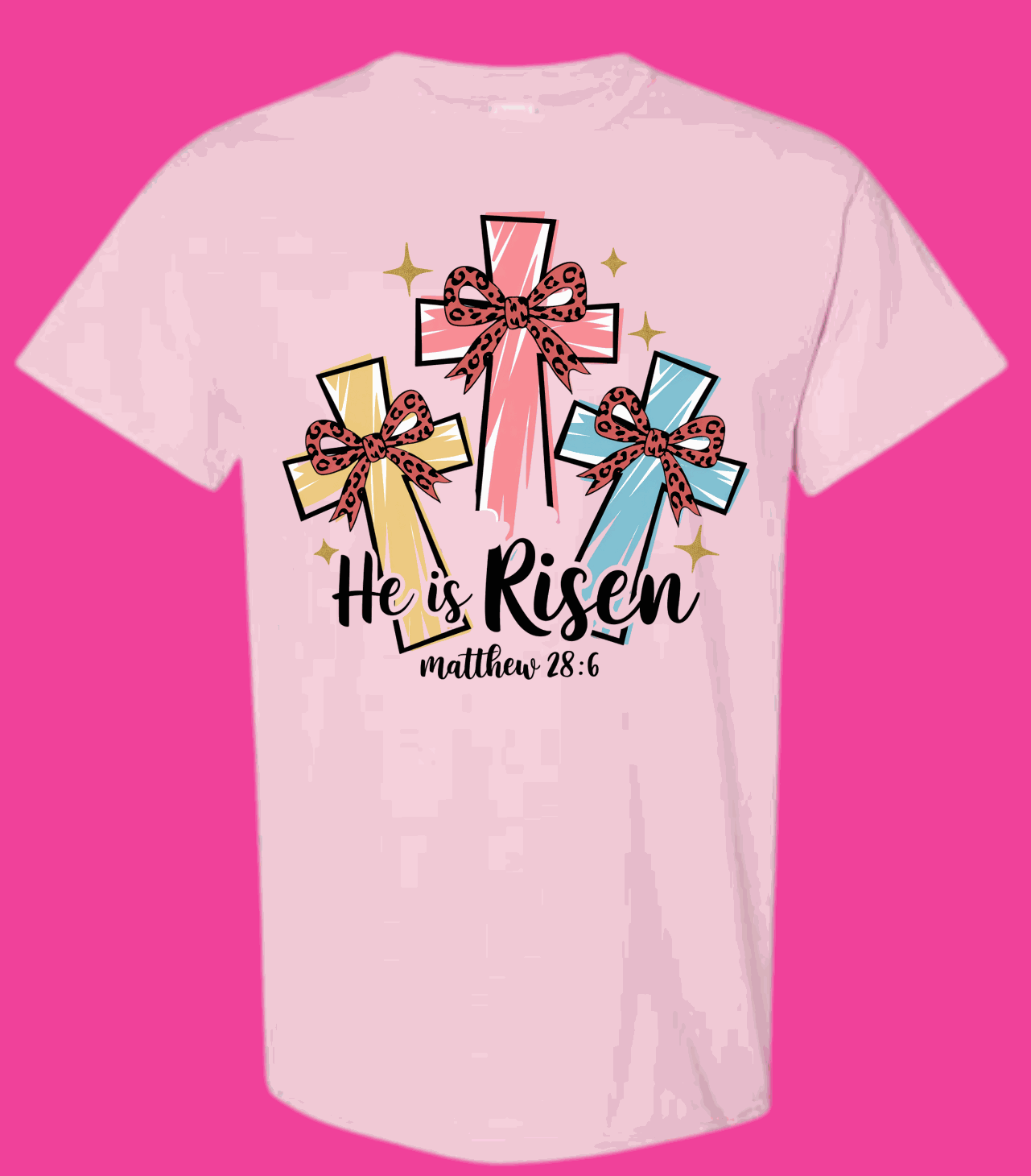Pink "He Is Risen" T-shirt featuring colorful crosses with bows and the text "Matthew 28:6," celebrating Easter with playful design.