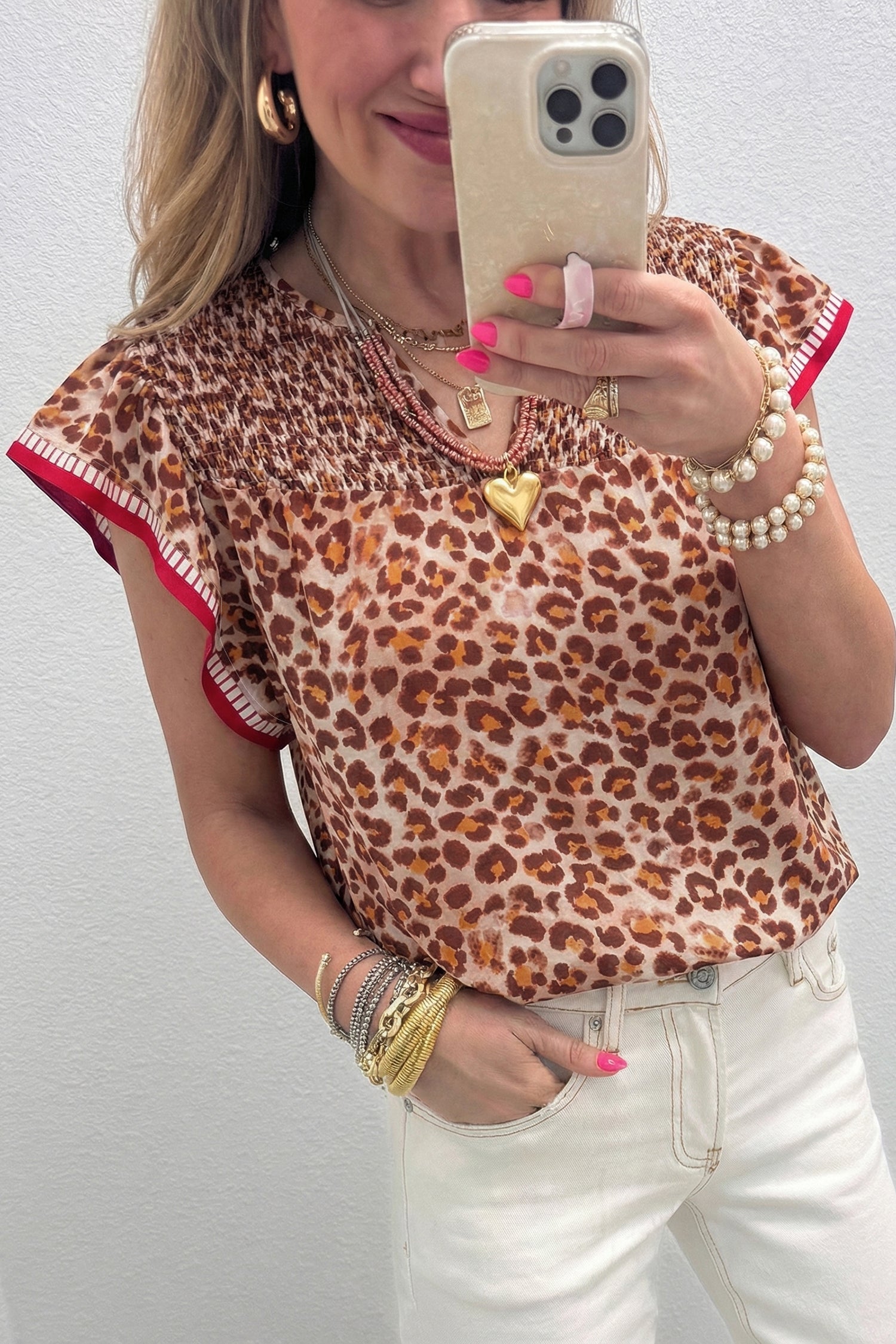 Apricot leopard blouse with red contrast trim - mirror selfie on model with cream jeans and gold jewelry showing smocked yoke and ruffle sleeve detail